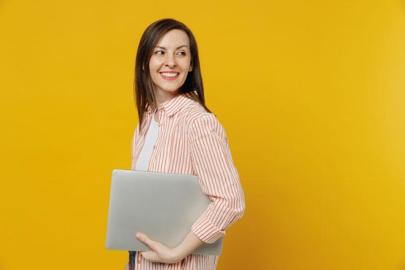 Femme souriante avec un ordinateur portable sur fond jaune