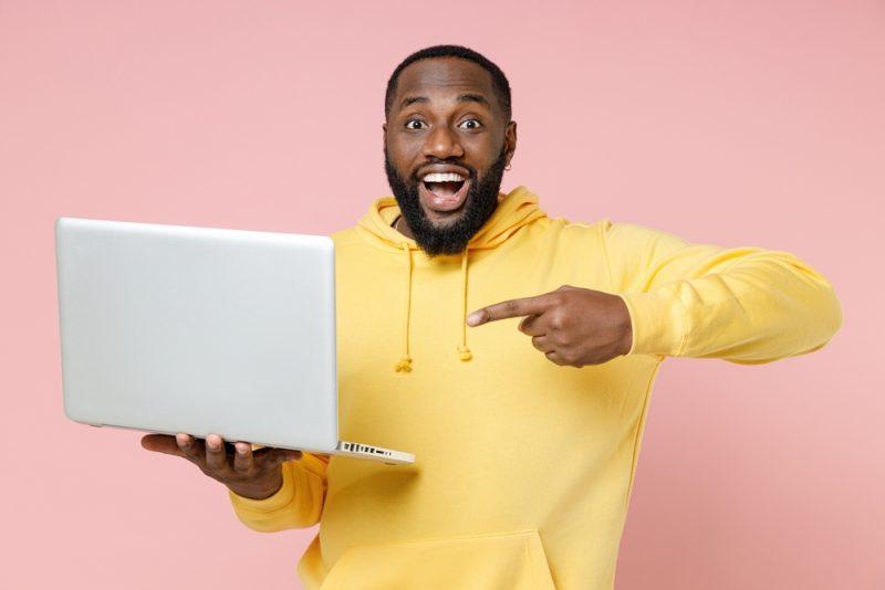 Homme souriant pointant un ordinateur portable, illustrant une idée de business SaaS rentable pour se lancer dans l’entrepreneuriat.